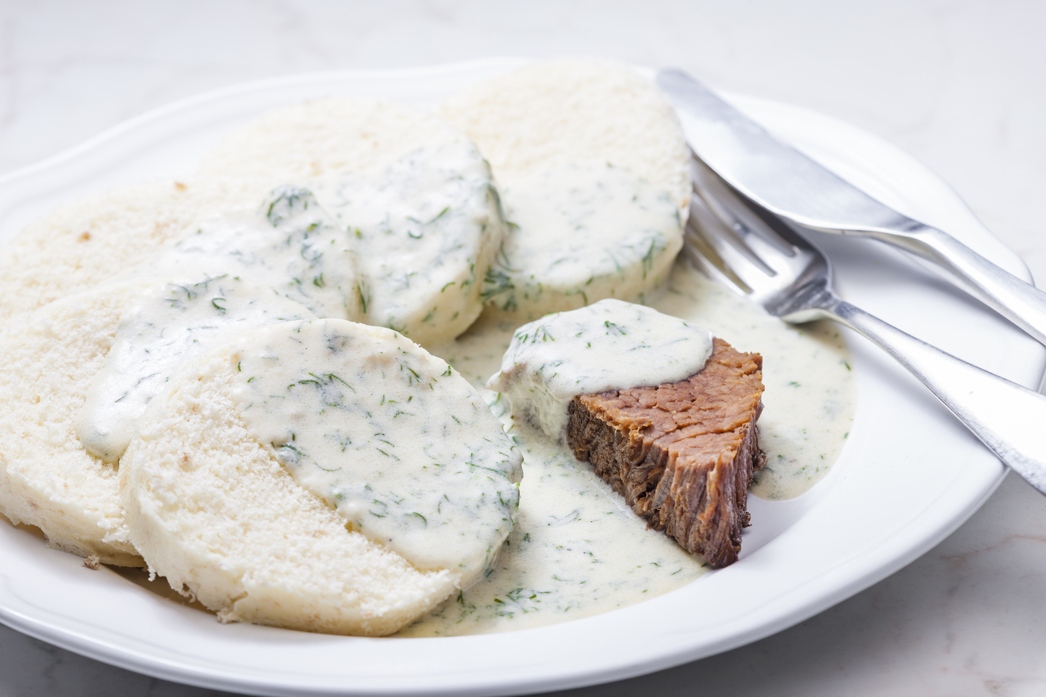 white dill sauce over meat and dumplings